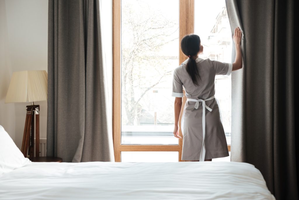 Female housekeeping opening window curtains